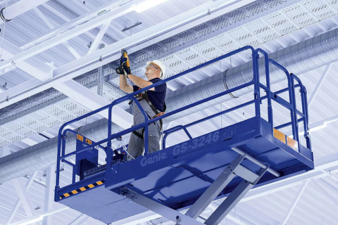 Employee on a scissor lift installing media supply on the ceiling of a factory.